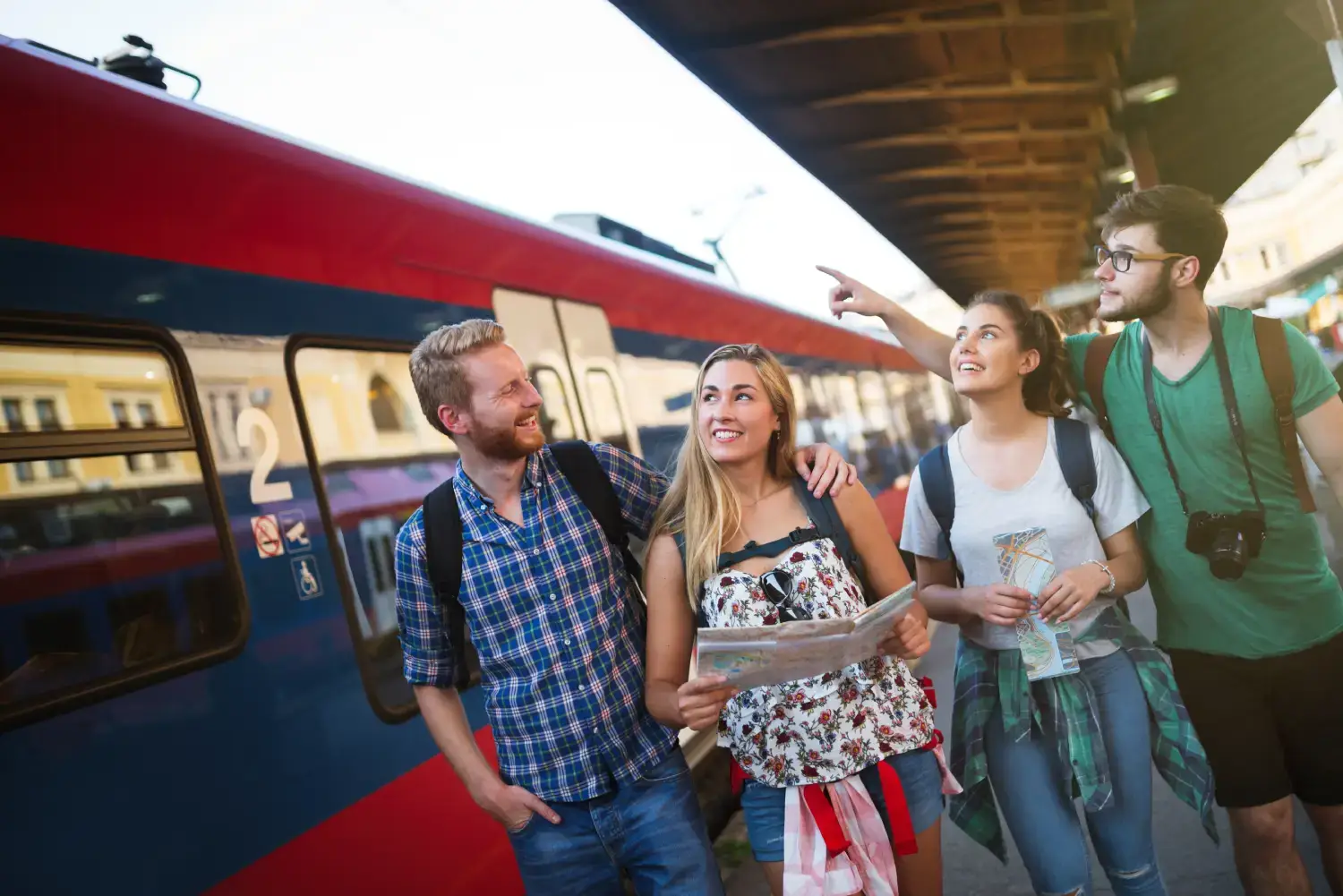 Jovens estudantes olhando as rotas de trem em um mapa com o trem ao lado.